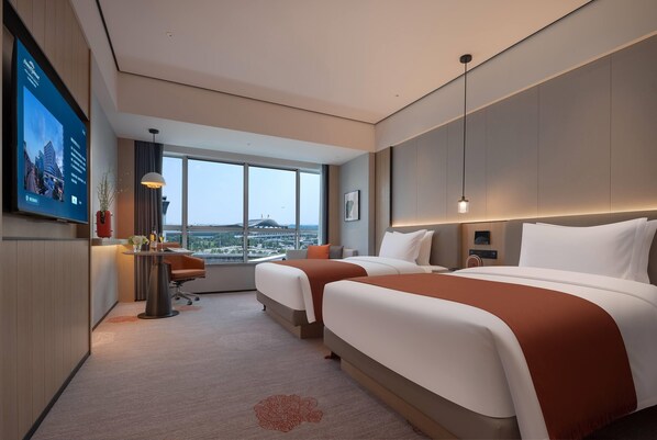 A hotel room with two beds, a desk, a TV, and a large window offering a city view. - Howard Johnson Airport Hotel Changsha (Changsha)