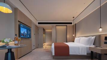A modern hotel room with a bed, bedside table, TV, and a small desk with a chair.