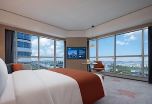 A modern hotel room with a large bed, a TV mounted on the wall, a small table with a chair, and a view of the city through large windows. - Howard Johnson Airport Hotel Changsha (Changsha)