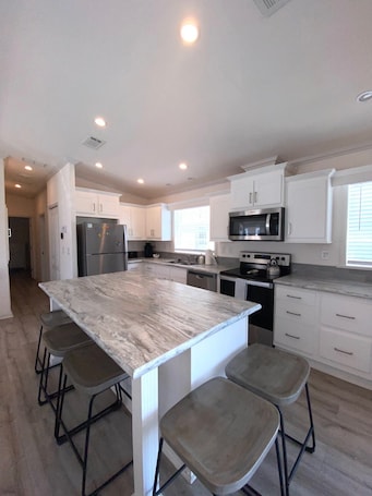 A modern kitchen with white cabinets, stainless steel appliances, and a marble island with bar stools.