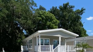 Une maison mobile de plain-pied, dotée d’un porche couvert et d’un petit jardin à l’avant.