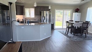 A spacious kitchen with a central island, dark wooden flooring, and a dining area with a table and chairs. - Spectacular Fully fenced 3 bedroom home  in Keaau with Amenities and Fast WiFi (Keaau)