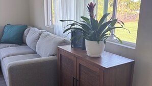 A living room with a grey sofa, a wooden cabinet, and a potted plant. - Spectacular Fully fenced 3 bedroom home  in Keaau with Amenities and Fast WiFi (Keaau)
