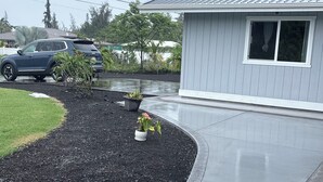 A residential driveway with a car parked on the left, a small shed on the right, and a landscaped garden area with potted plants. - Spectacular Fully fenced 3 bedroom home  in Keaau with Amenities and Fast WiFi (Keaau)