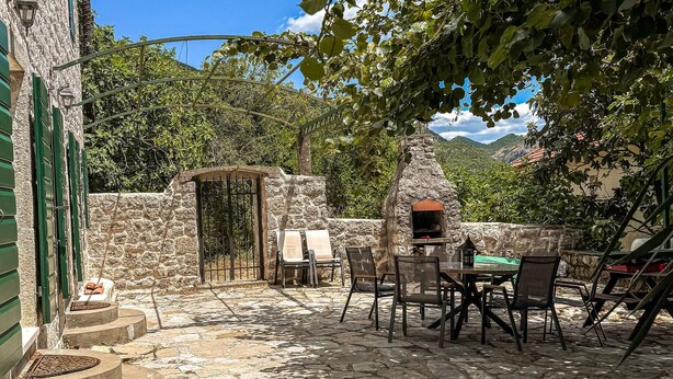 An outdoor patio with stone flooring, a table with chairs, a stone wall, and a view of mountains in the background. - Luxurious home in Herceg Novi (Herceg Novi)