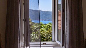 A room with a sliding glass door leading to a balcony overlooking a body of water and a hilly landscape. - Luxurious home in Herceg Novi (Herceg Novi)