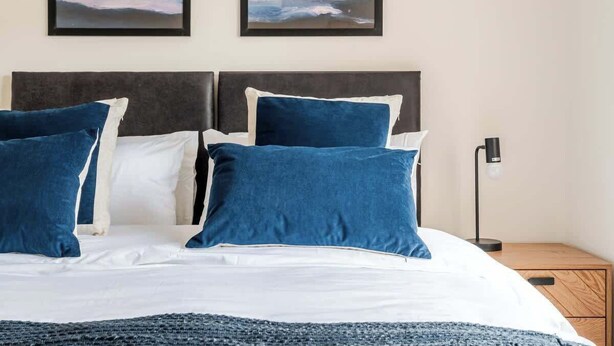 Ein Bett mit weißer und blauer Bettwäsche, ein dunkles Kopfteil und zwei gerahmte Kunstwerke darüber.