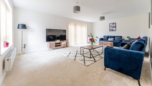Ein Wohnzimmer mit Fernseher, blauen Sofas, einem Couchtisch und einem großen Fenster.