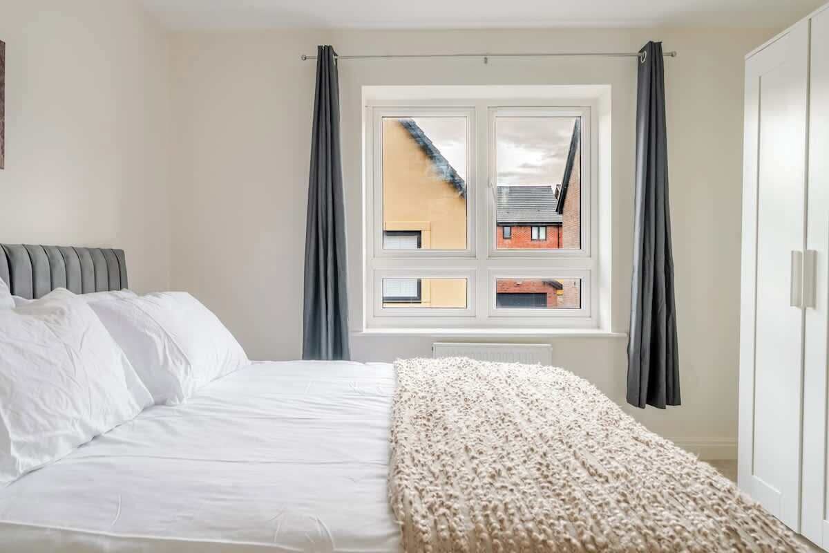 A bedroom with a bed, a window, and a view of buildings outside.