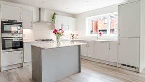 A modern kitchen with white cabinetry, a central island, a built-in oven, and a window providing natural light. - Spacious 4 Bed Contractor & Family Home, Bristol (Stoke Gifford)