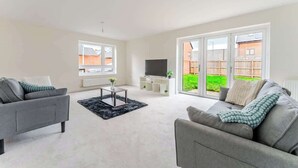 A spacious living room with a grey sofa, a coffee table, and a TV. - Spacious 4 Bed Contractor & Family Home, Bristol (Stoke Gifford)