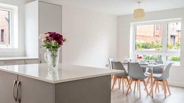 A modern kitchen with a central island, grey chairs, and a vase of flowers. - Spacious 4 Bed Contractor & Family Home, Bristol (Stoke Gifford)