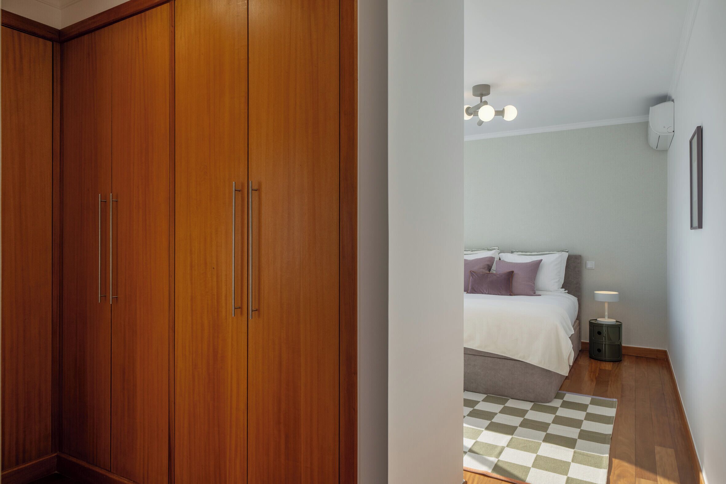 A bedroom with a bed, bedside table, and a checkered rug.