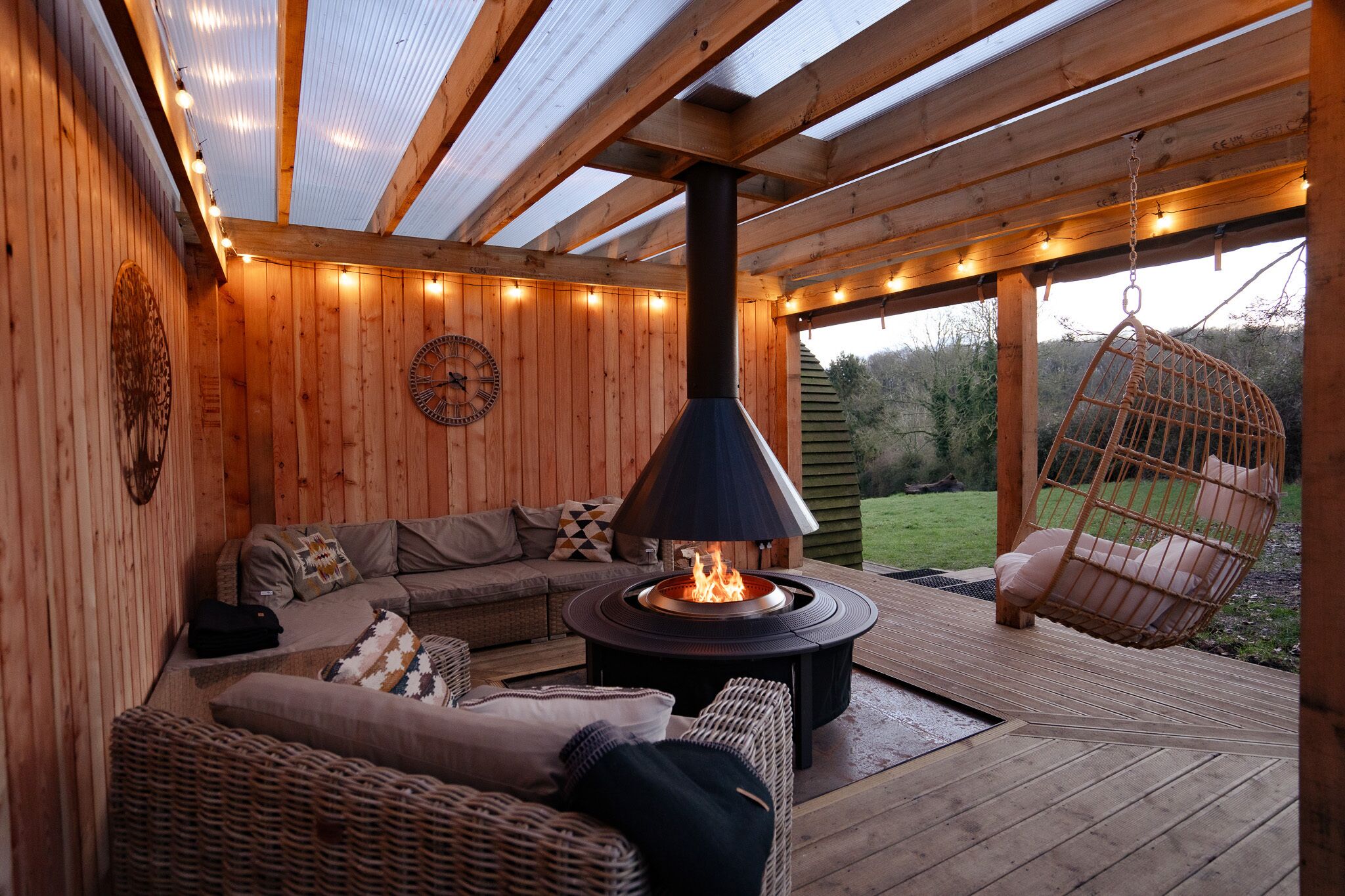 Eine Holzterrasse mit einer Couch, einem Hängesessel und einer Feuerstelle.