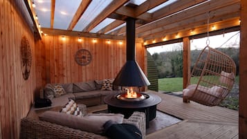 Eine Holzterrasse mit einer Couch, einem Hängesessel und einer Feuerstelle.