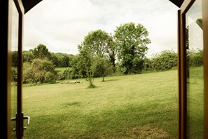 A view from inside a room looking out onto a grassy field with trees and a fence. - Luxury Cabin with Pergola in Rural Hampshire (Chawton)
