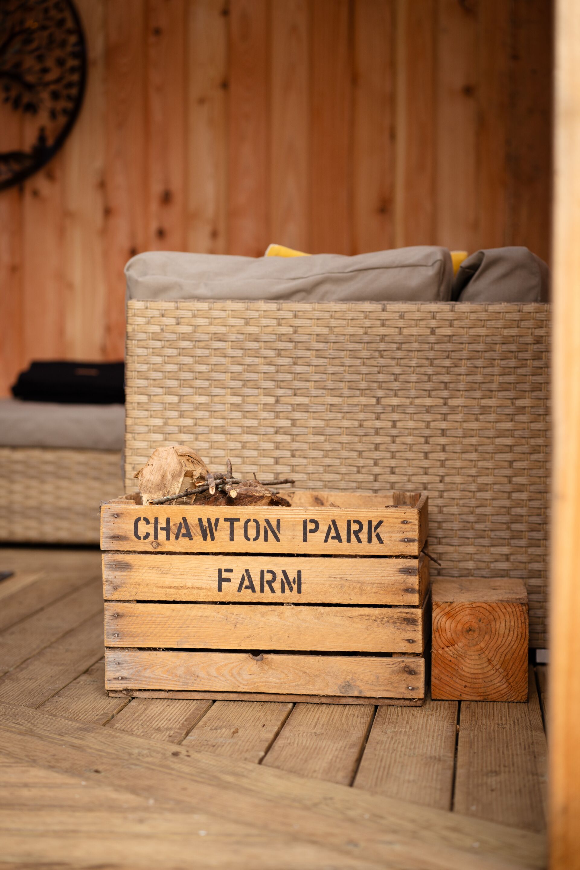 Een houten kist met de tekst 'CHAWTON PARK FARM', geplaatst op een houten vloer met een rieten bank op de achtergrond.