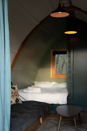 A cozy, small room with a bed, a small table, and a window. - Luxury Cabin with Pergola in Rural Hampshire (Chawton)