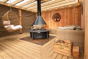A cozy outdoor seating area with a hanging chair, a sofa, and a wood-burning stove. - Luxury Cabin with Pergola in Rural Hampshire (Chawton)