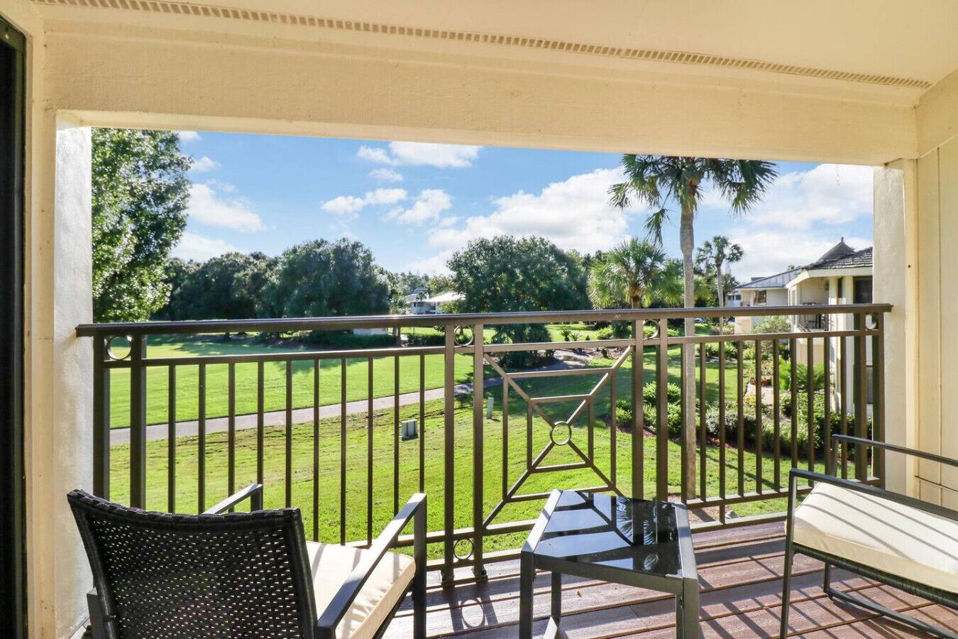 A balcony with a view of a golf course, a table, and two chairs.