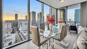 A modern dining area with a glass table and chairs, a vase with red flowers, and a city view through large windows. - Cosy 3Beds/3Baths High Floor Unit Heart Of Miami (Miami)
