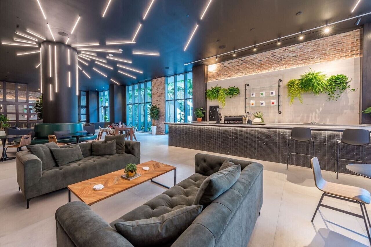 A modern lounge area with sofas, a coffee table, and a bar with a brick wall and plants.