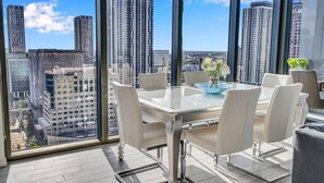 Een hoog appartement met een glazen eettafel en stoelen, een vaas met bloemen en uitzicht op de stad.