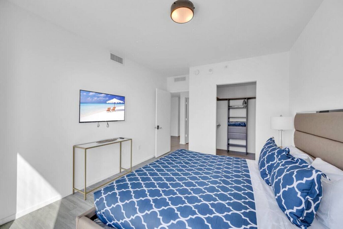 Un dormitorio moderno con cama, televisor, armario y puerta que da a otra habitación.