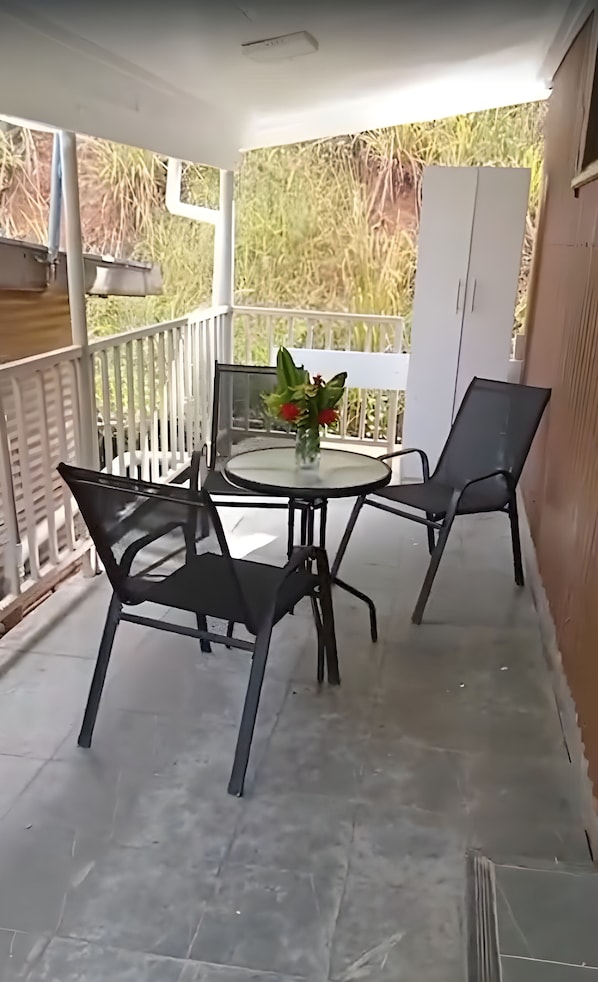 Un pequeño patio al aire libre con una mesa redonda y dos sillas, una planta en maceta y un armario blanco.