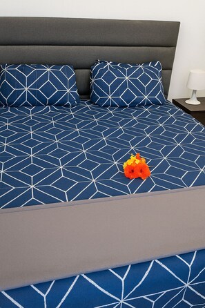 Una cama con un estampado geométrico azul y blanco, dos almohadas a juego y un pequeño ramo de flores naranjas.