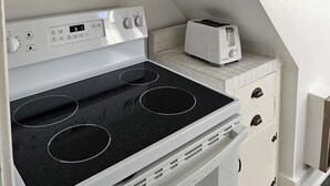 Une cuisine avec un fourneau blanc, un grille-pain et une petite étagère sur laquelle est posé un vase.