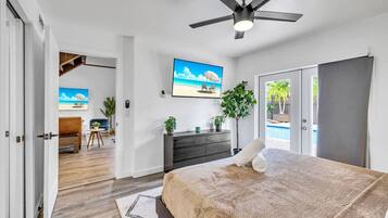A bedroom with a bed, a ceiling fan, a TV, a dresser, and a view of the outside.