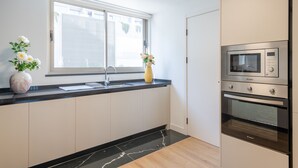 Moderni keittiö, jossa on musta työtaso, valkoiset kaapit, ikkuna, jossa on sälekaihtimet, mikroaaltouuni ja uuni.