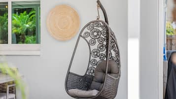 A hanging chair with a circular woven seat and backrest, a woven wall hanging, and a window with a view of greenery.