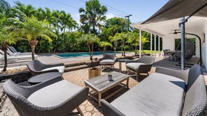 Zona junto a la piscina con mobiliario de mimbre, una mesa y un espacio de descanso cubierto.