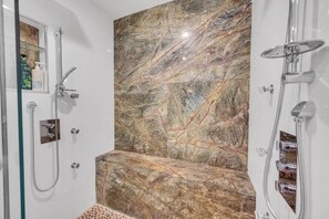 A bathroom with a marble wall, a glass shower enclosure, and a showerhead. - Amazing house with pool (Miami)