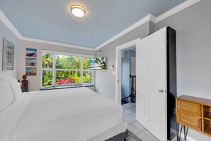 A bedroom with a large bed, a window with a view of greenery, and a wooden dresser. - Amazing house with pool (Miami)