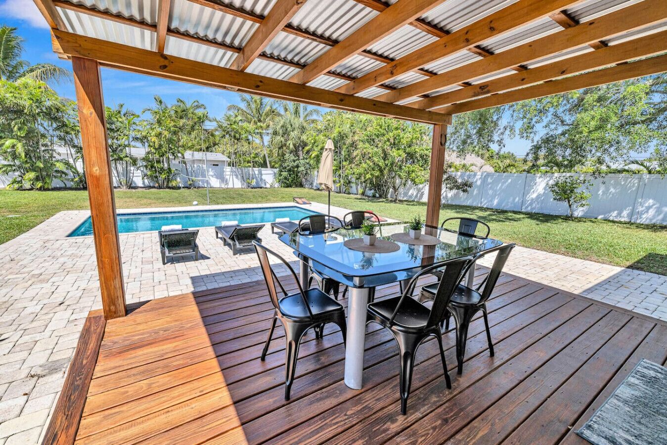 An outdoor patio with a glass table and chairs, a pool, and a wooden deck.