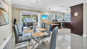 Een moderne keuken met een glazen eettafel, donkere kastjes en uitzicht op het buitengebied.