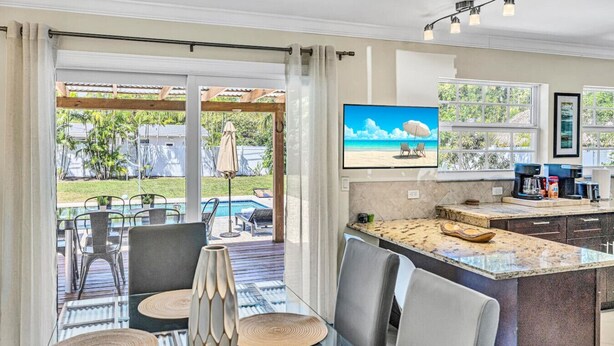 Een moderne keuken met een groot eiland, een eethoek met uitzicht op het zwembad, en een aan de muur bevestigde televisie.