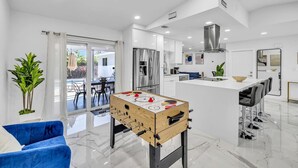 A modern kitchen with a foosball table, a dining area with a blue sofa, and a view to the outside. - Amazing house with pool (Delray Beach)