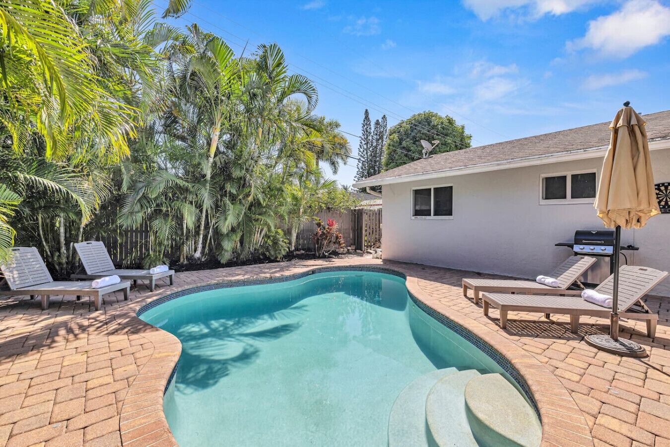 A backyard with a swimming pool, lounge chairs, and a barbecue grill.
