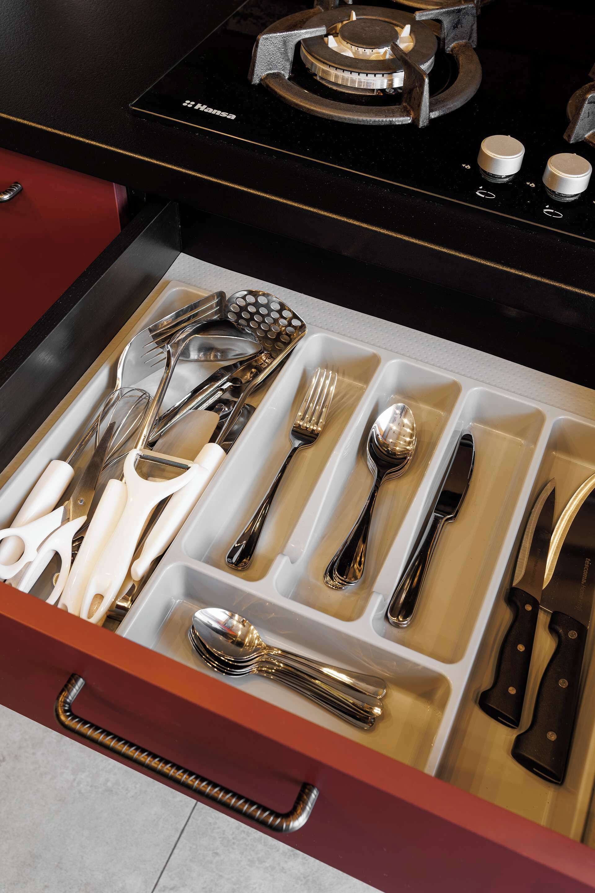 A drawer with neatly organized cutlery including forks, knives, spoons, and a grater.