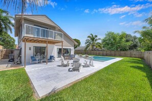Ein zweistöckiges Haus mit überdachter Terrasse, Swimmingpool und gepflegtem Rasen.