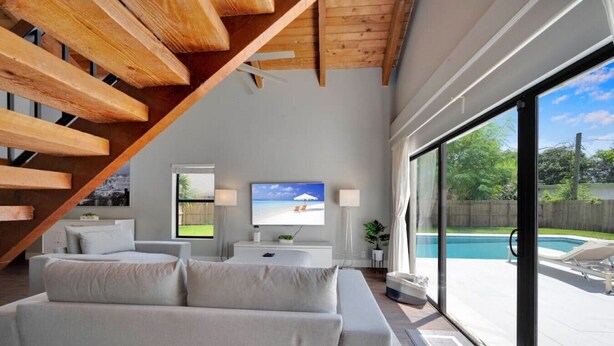 Een moderne woonkamer met een trap, een televisie en uitzicht op een zwembad.