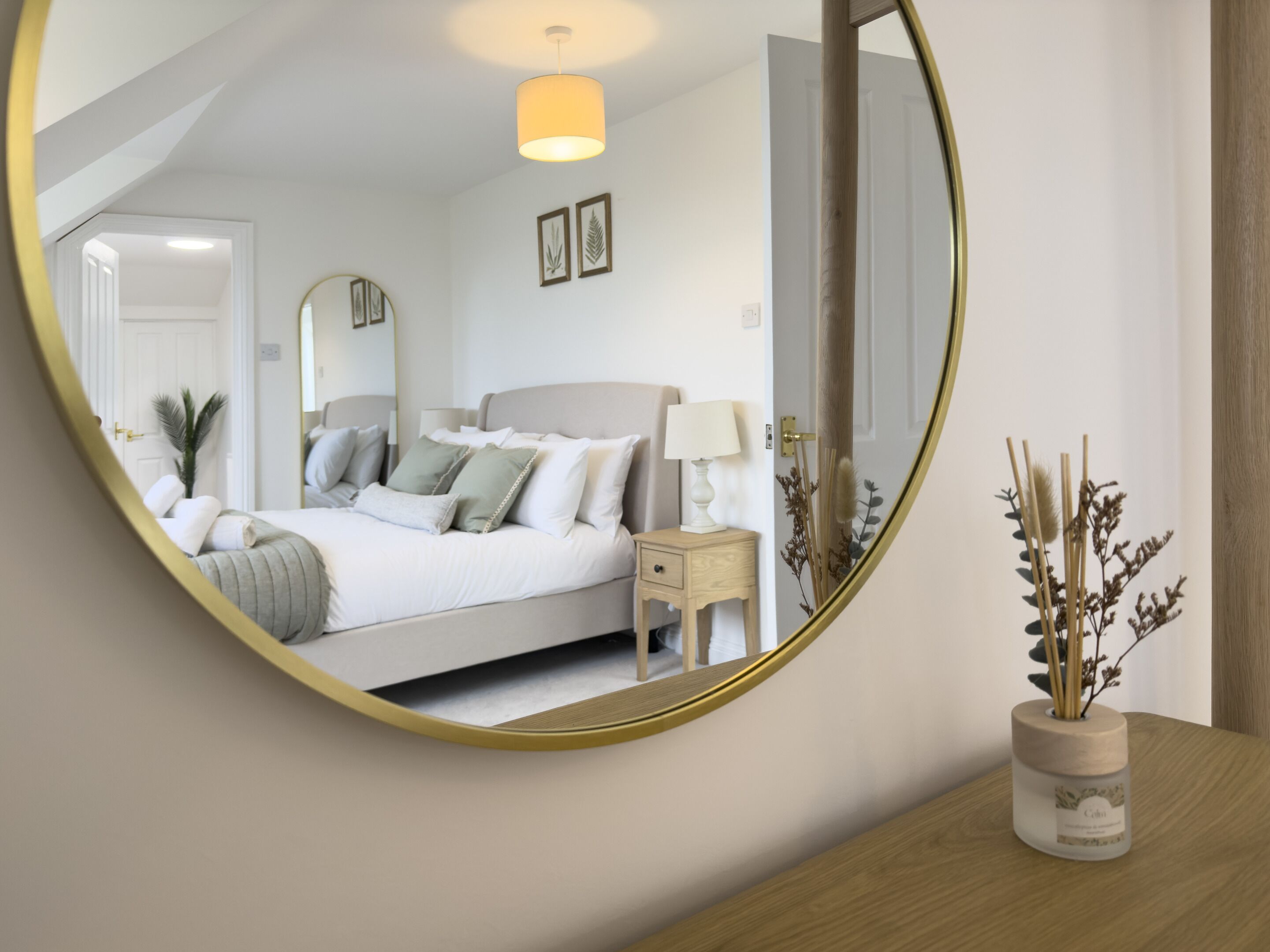 A bedroom with a bed, bedside table, lamp, and a mirror on the wall.