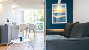 Ett modernt vardagsrum med en mörkblå accentvägg, en soffa, en matplats med bord och stolar samt ett köksområde med ett skåp och en lampa.