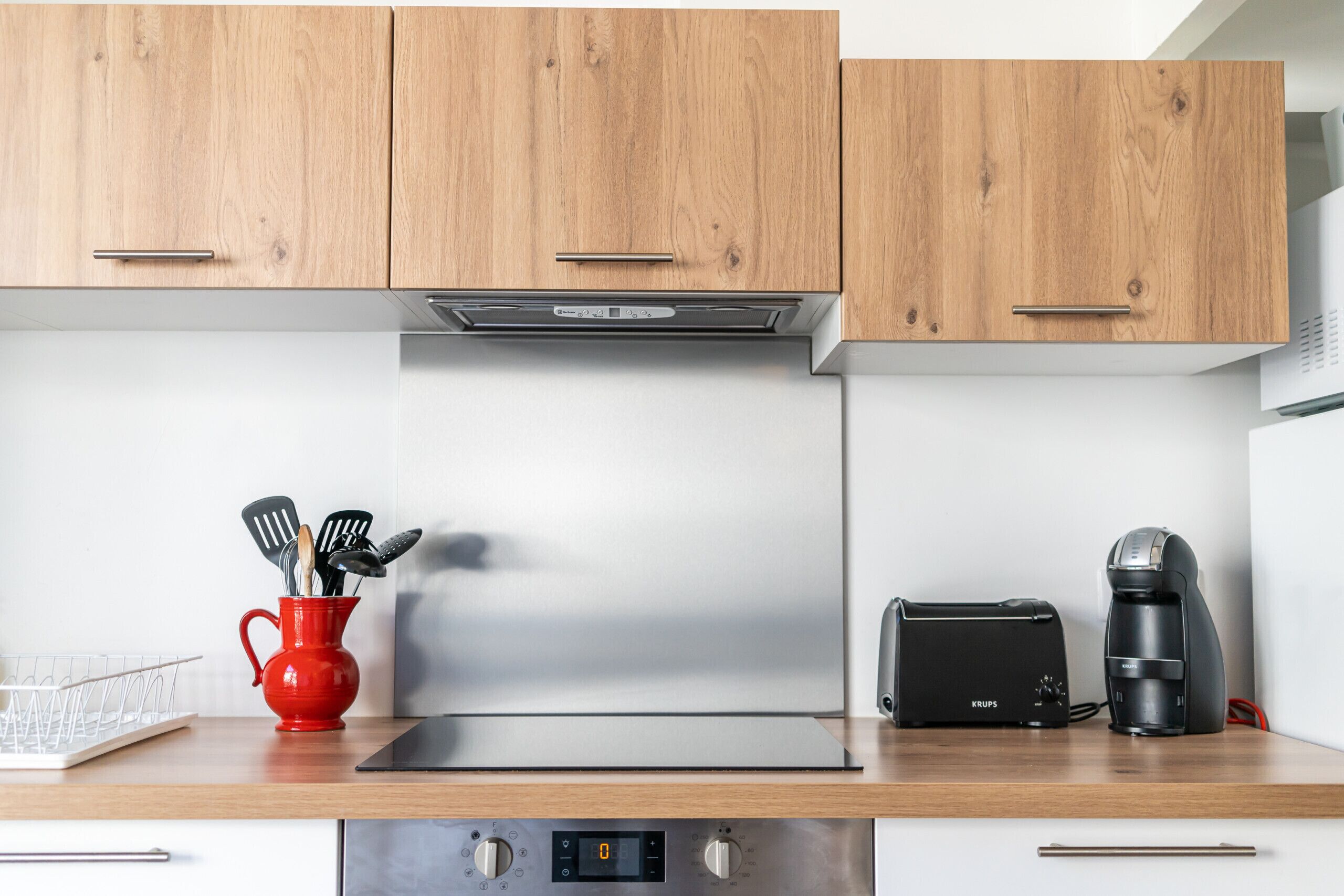 A kitchen with wooden cabinets, a stainless steel range hood, a red mug with utensils, a toaster, and a coffee maker.