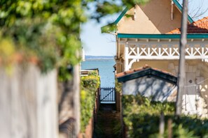 A narrow pathway leading to a building with a white facade and green trim. - [Élégant] Duplex Centre-Ville Accès privé Plage (Arcachon)