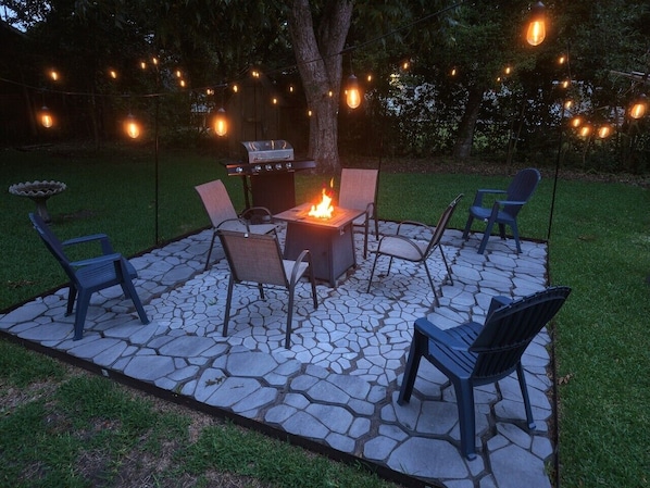 Un patio al aire libre con un hogar a leña de piedra, sillas y una parrilla.